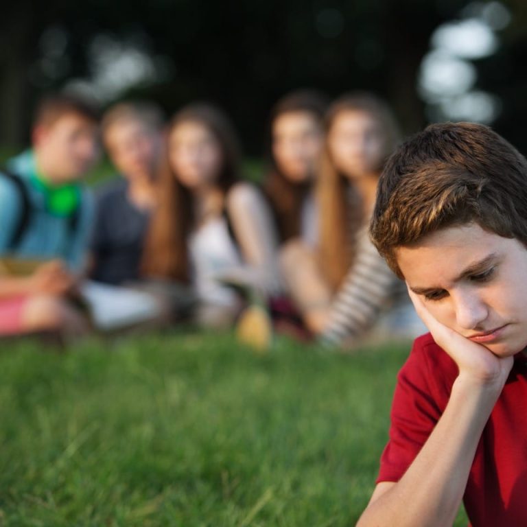 Teenage-boy-feeling-sad-being-watched-by-a-group-of-friends-in-the-background